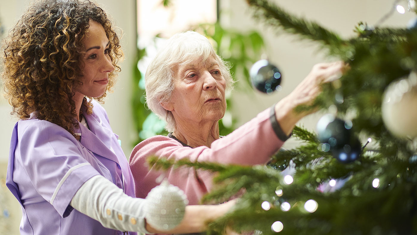 Make the Holiday Season Memorable image of a resident and a caregiver dressing a tree.