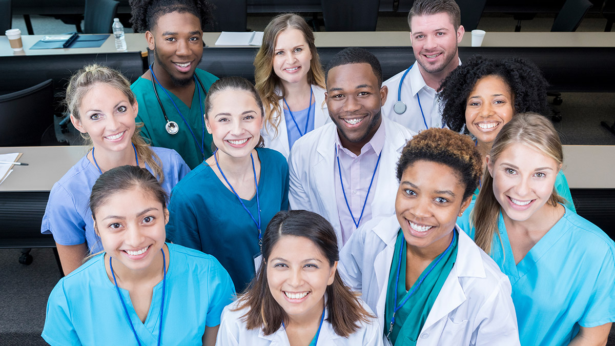 Diverse group of smiling skilled nursing care workers in scrubs and lab coats gathered together, representing a multidisciplinary long-term care team.