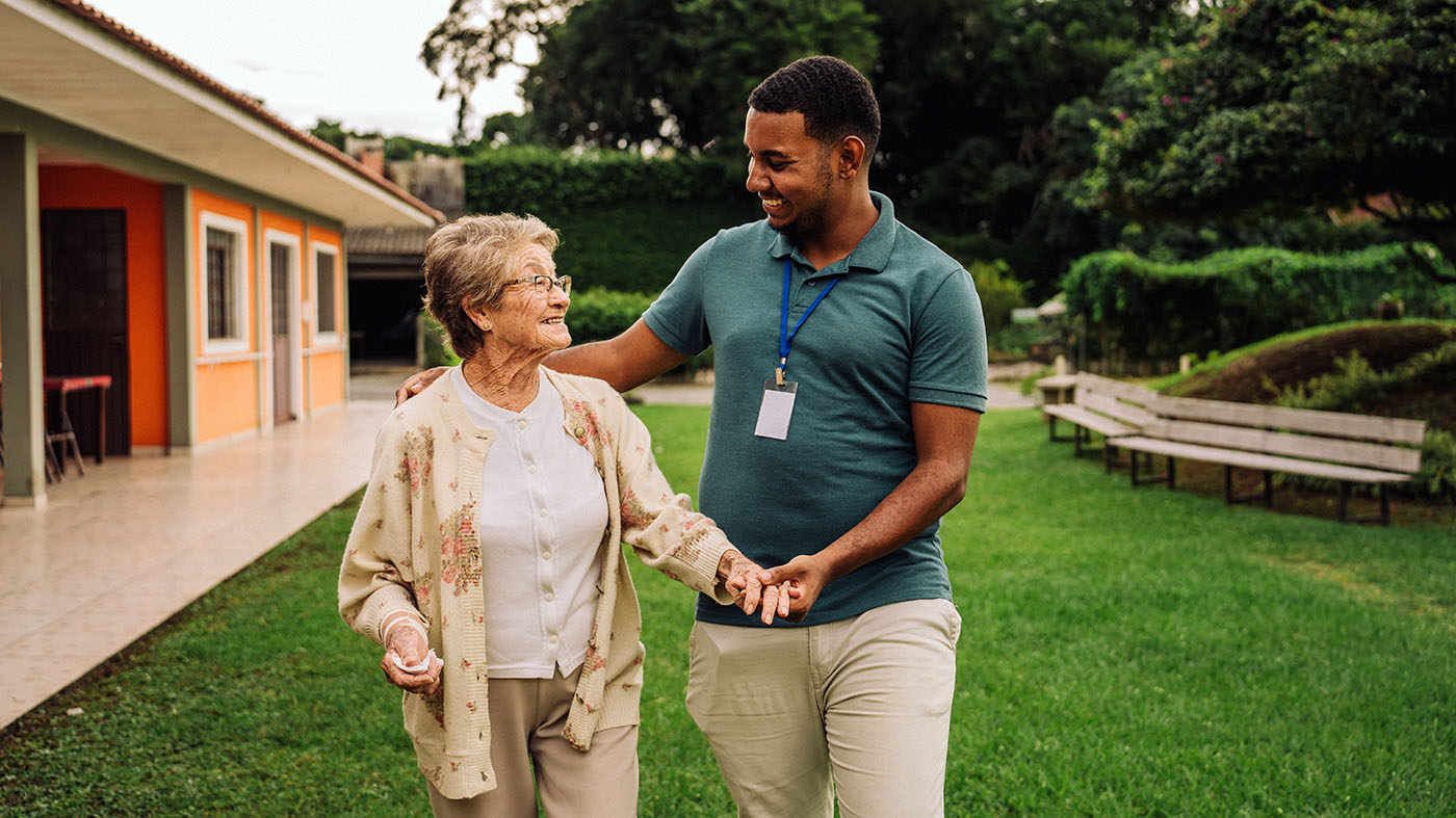 Social worker and elderly resident walking outdoors at a skilled nursing facility, illustrating person-centered social services in skilled nursing facilities.
