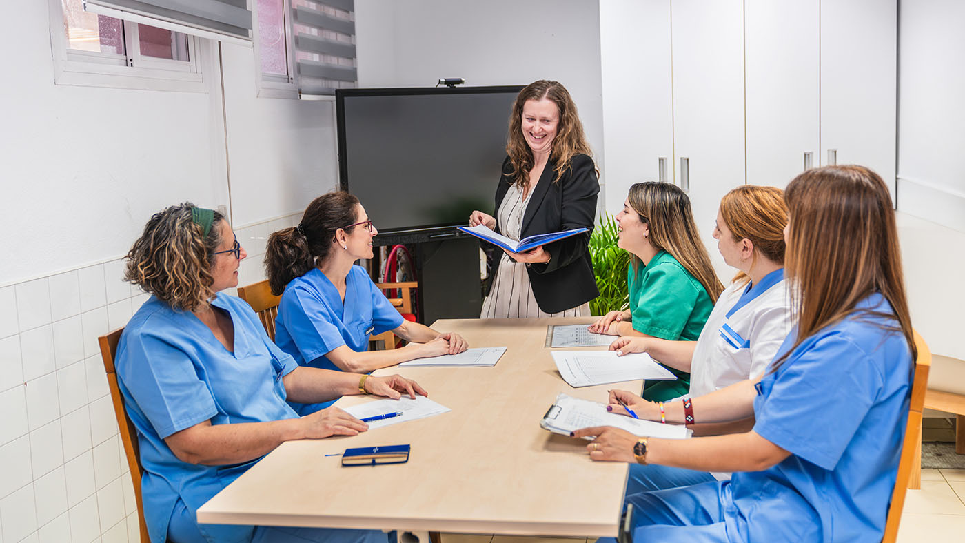 Facility administrator presenting updated materials during a policy and procedure review meeting with nursing staff in a skilled nursing facility